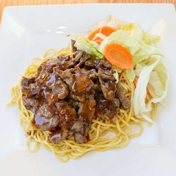 Teriyaki beef with noodles, cabbage, and carrots on a white rectangular plate.