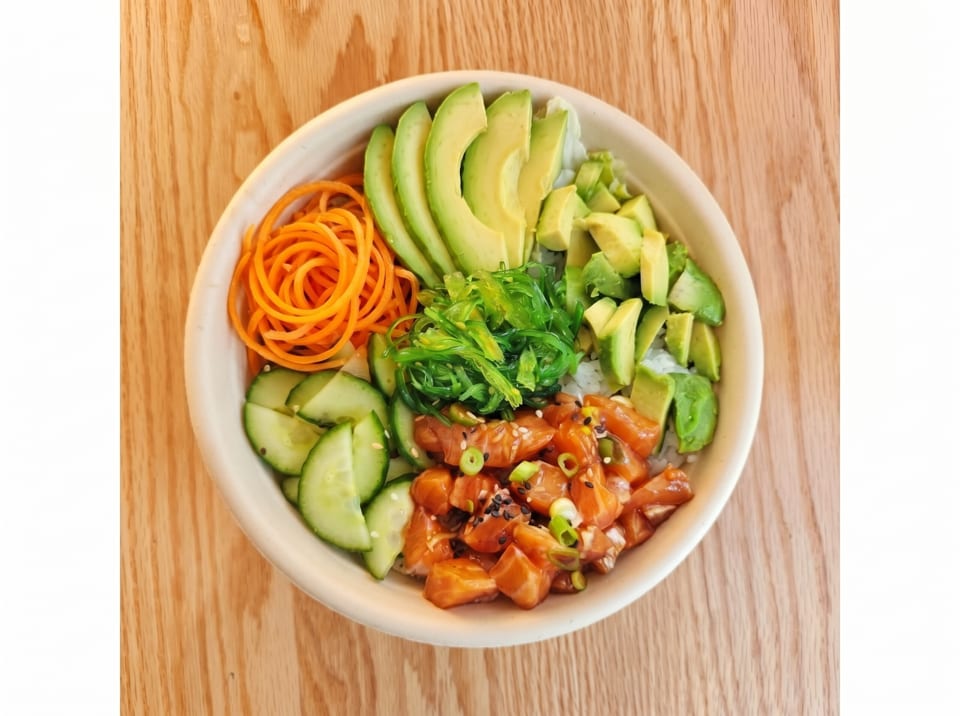 A colorful poke bowl with salmon, avocado, seaweed, carrots, and cucumber on a wooden table.