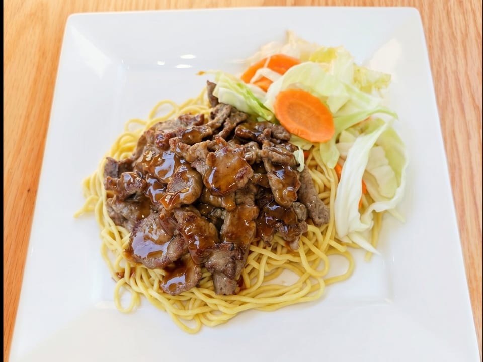 Teriyaki beef with noodles, cabbage, and carrots on a white rectangular plate.