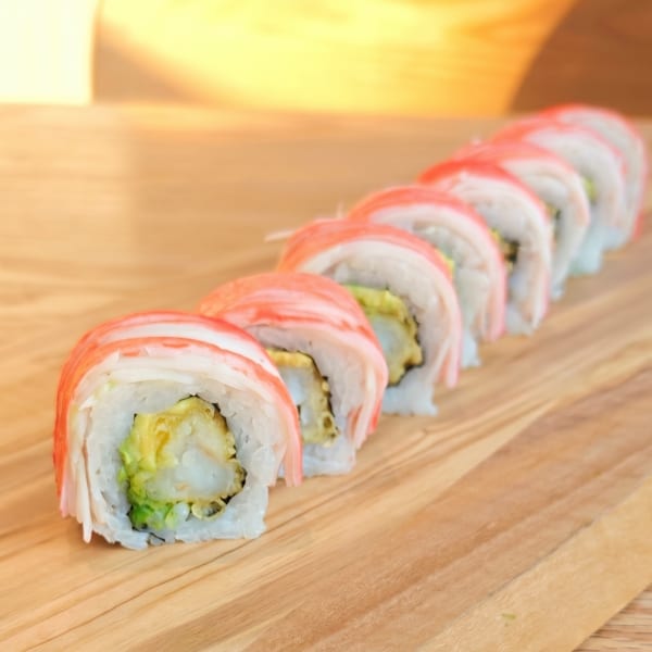A row of crab and avocado sushi rolls on a light wooden cutting board.