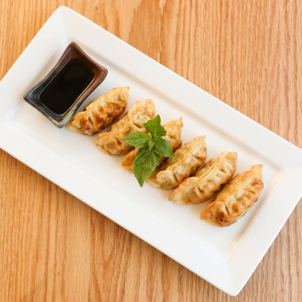 Golden-brown fried dumplings with a small bowl of soy sauce and basil garnish on a white plate.