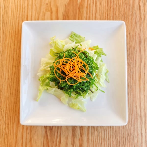 A fresh seaweed salad with shredded carrots and lettuce on a white square plate.