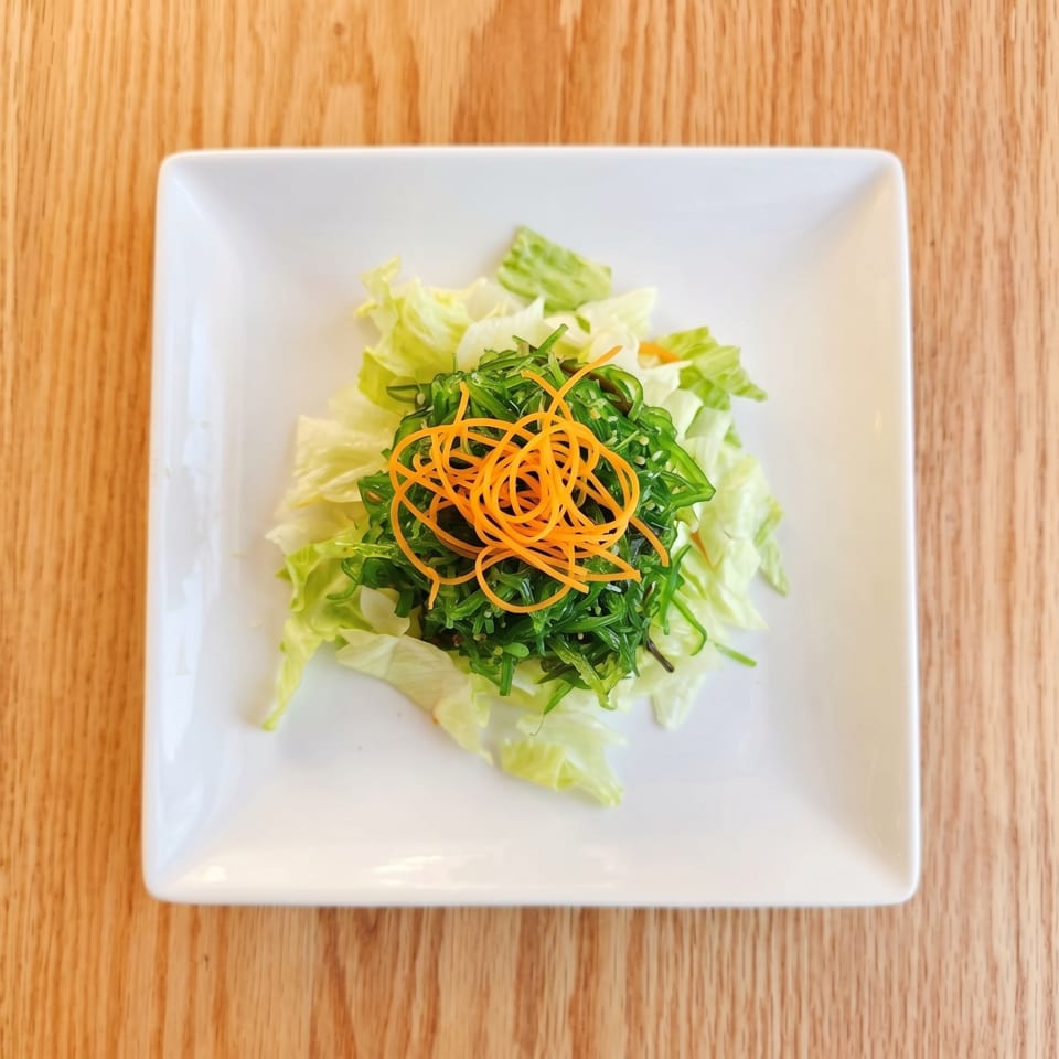 A fresh seaweed salad with shredded carrots and lettuce on a white square plate.
