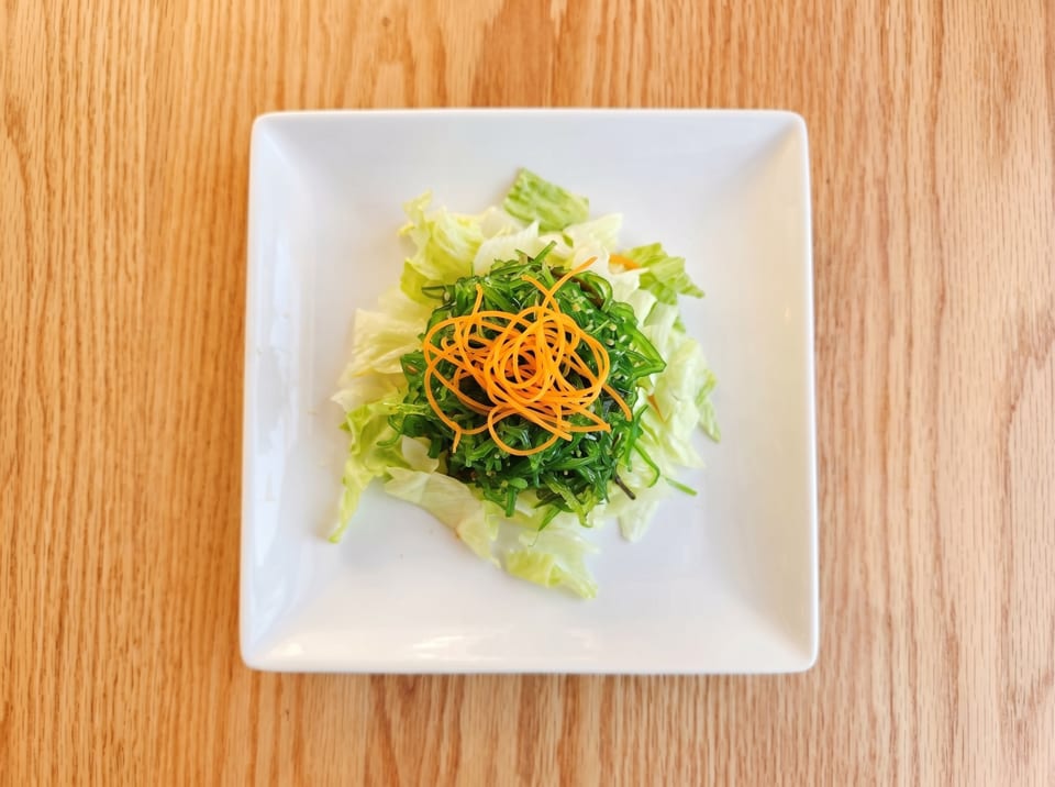 A fresh seaweed salad with shredded carrots and lettuce on a white square plate.