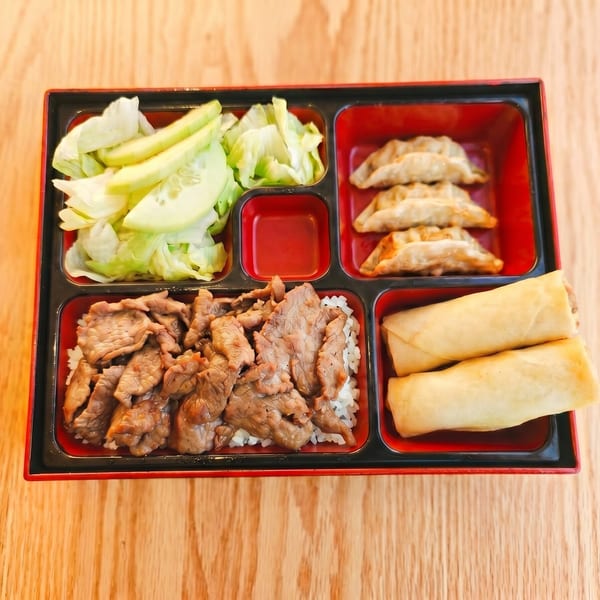 A bento box with beef and rice, dumplings, spring rolls, and a side salad.