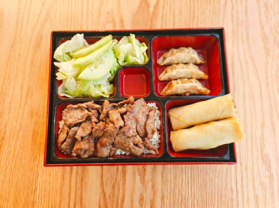 A bento box with beef and rice, dumplings, spring rolls, and a side salad.
