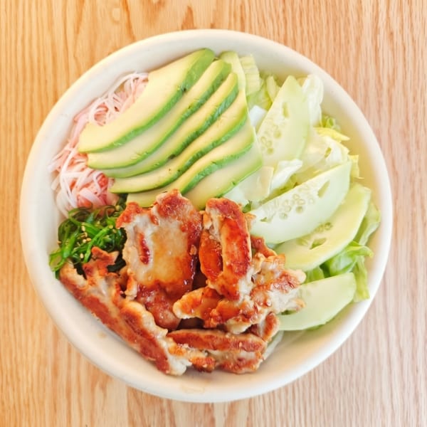 Top-down view of a poke bowl with grilled chicken, avocado, cucumber, and seaweed salad.