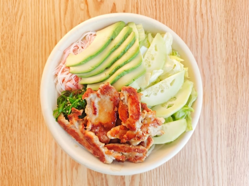 Top-down view of a poke bowl with grilled chicken, avocado, cucumber, and seaweed salad.