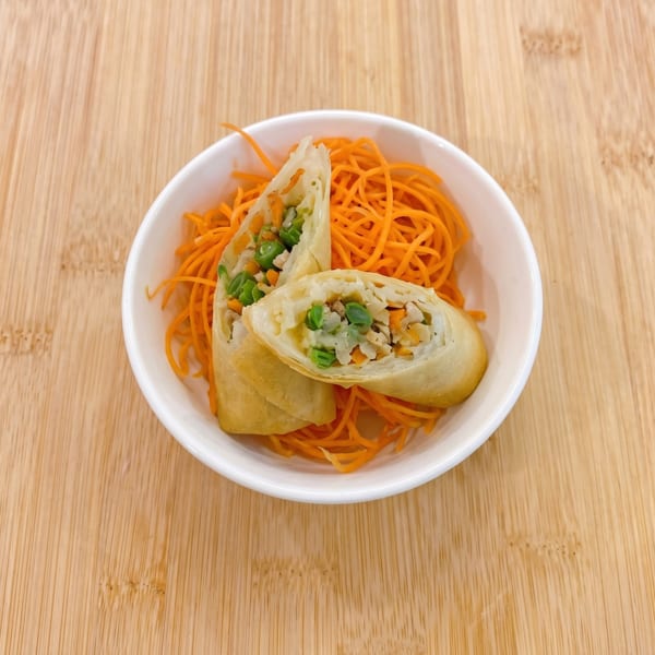 Two spring rolls, cut in half to show the vegetable and meat filling, served with shredded carrots.
