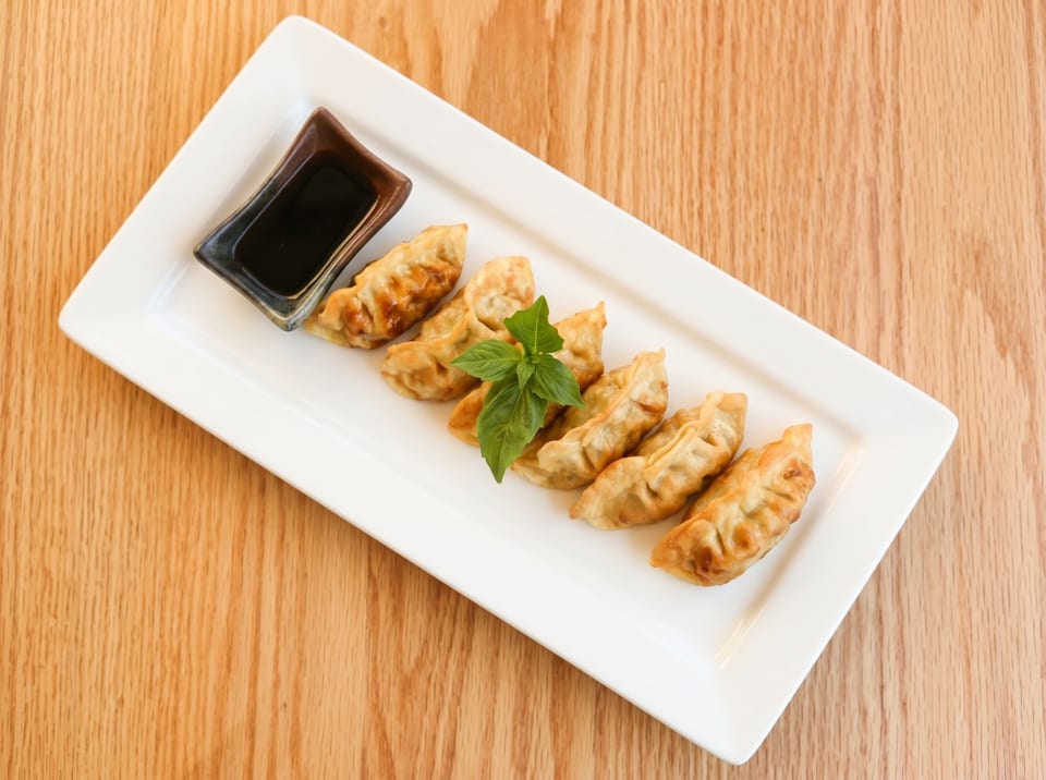 Golden-brown fried dumplings with a side of soy sauce and a basil garnish on a white plate.