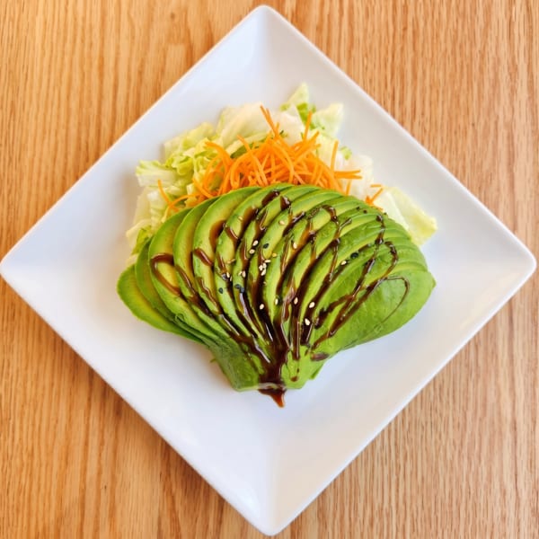 Avocado salad with shredded lettuce, carrots, balsamic glaze, and sesame seeds on a white plate.