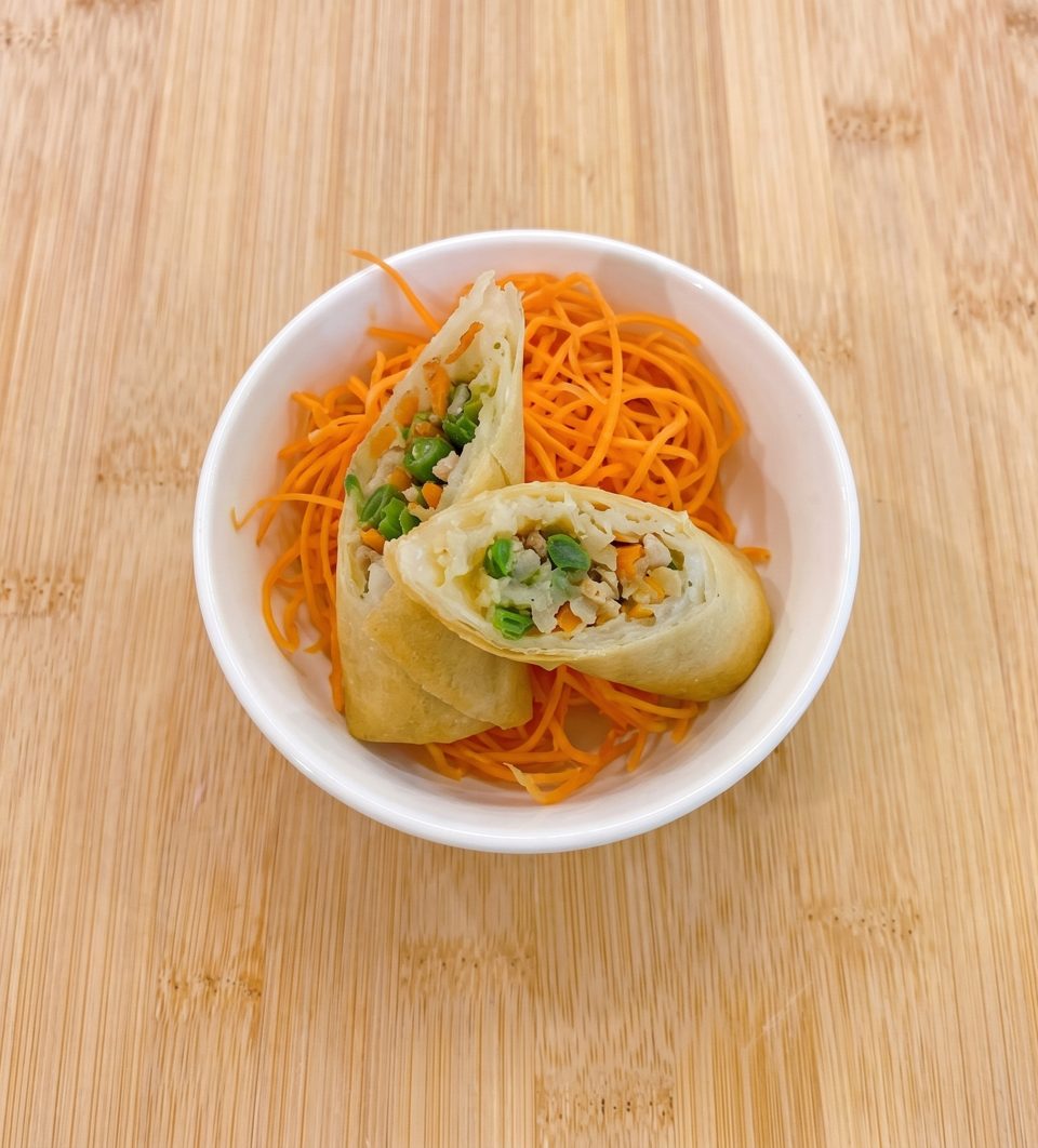 Two spring rolls, cut in half to show the vegetable and meat filling, served with shredded carrots.