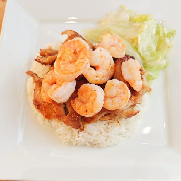 Grilled shrimp and chicken over white rice with a side of lettuce on a white plate.