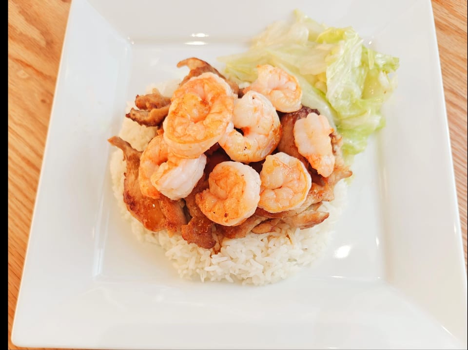 Grilled shrimp and chicken over white rice with a side of lettuce on a white plate.