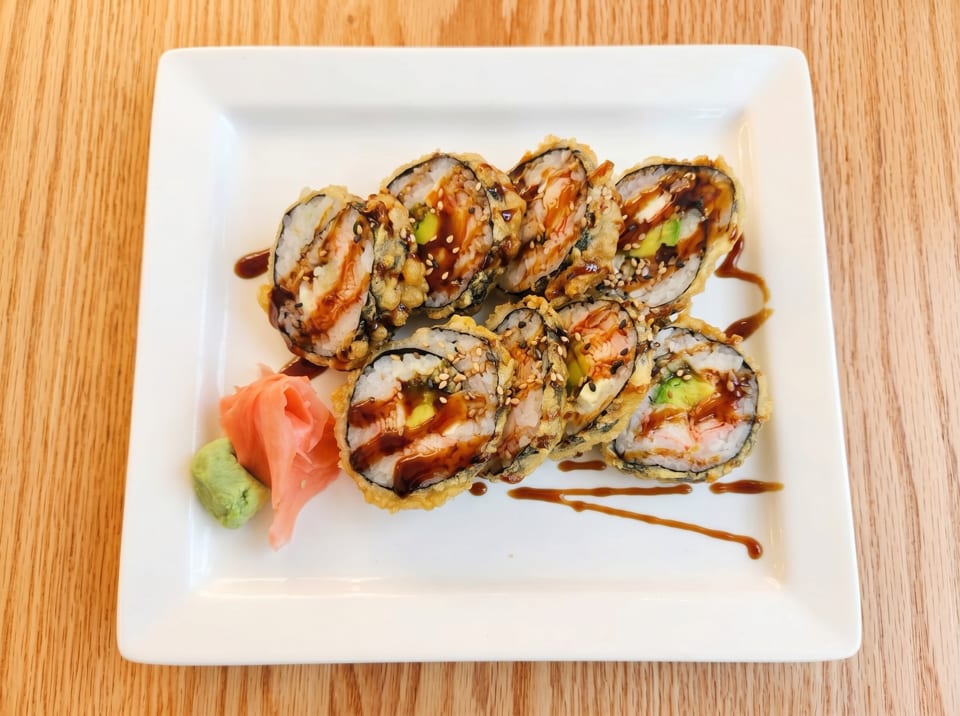 Tempura-fried sushi rolls with eel sauce, sesame seeds, avocado, and shrimp, served with ginger and wasabi.